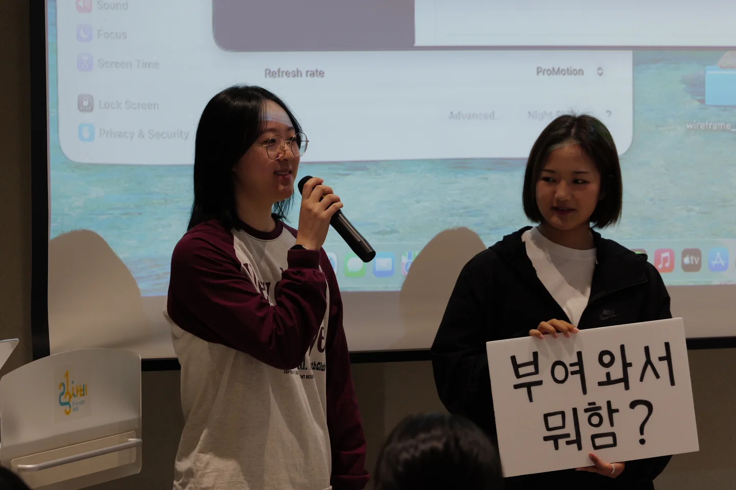 ‘부여 와서 뭐함?’ 플래카드를 들고 마이크 앞에서 설명하는 두 학생
