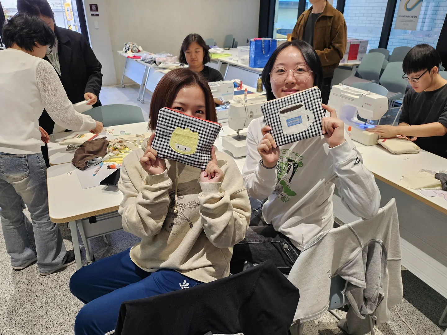 완성한 파우치를 얼굴 옆에 들어 보이는 두 학생